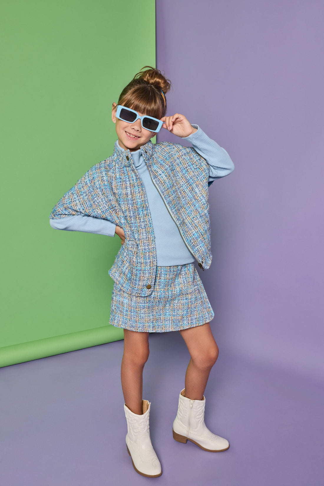 Model can be seen wearing a tweed cape in a blue tweed pattern. Cape pairs back with the matching tweed skort and ribbed turtleneck underneath to complete the look.