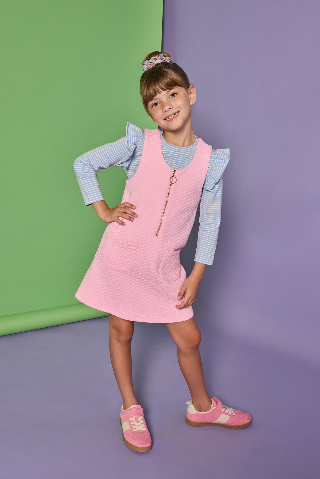 Model can be seen wearing a blue and white stripe long sleeve knit top with ruffles at the sleeves paired under a bubblegum pink quilted jumper. Jumper features quarter zip zipper down front and pockets. 