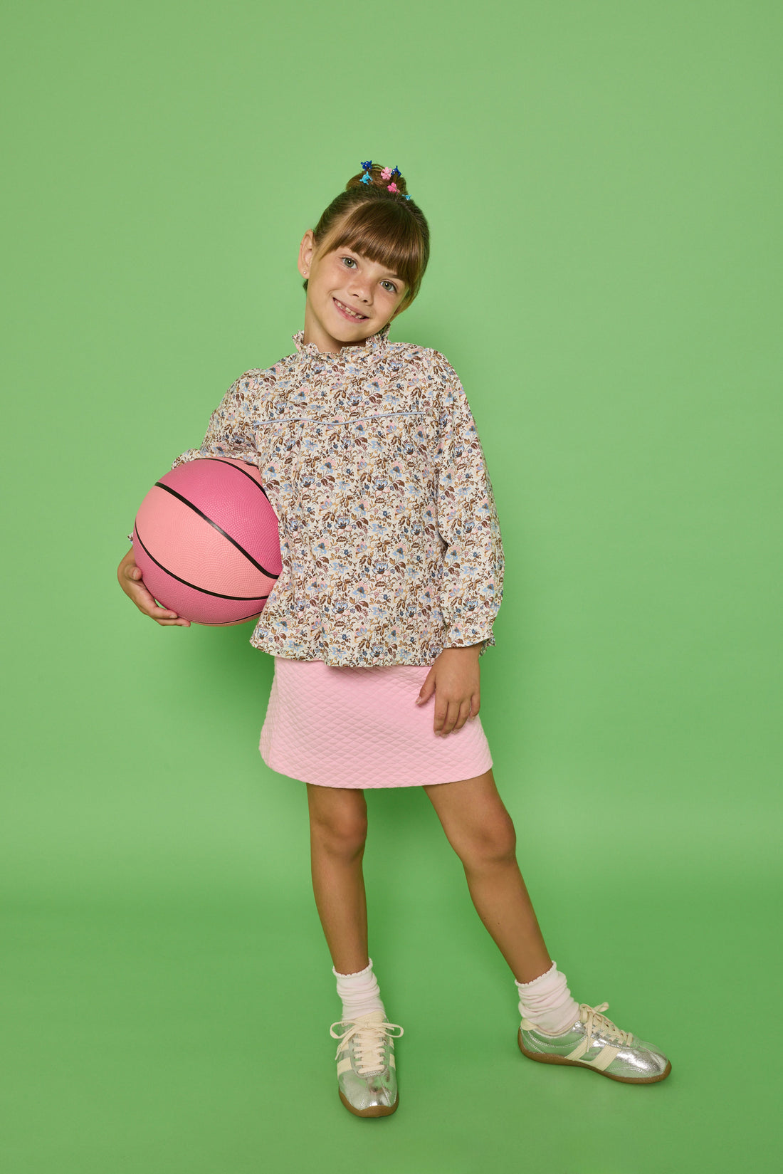 Model can be seen wearing a woven top with a ruffle neckline and button closure along back. The brown/pink/blue floral print pairs back perfectly with our quilted knit mini skirt in bubblegum pink to complete the look. 
