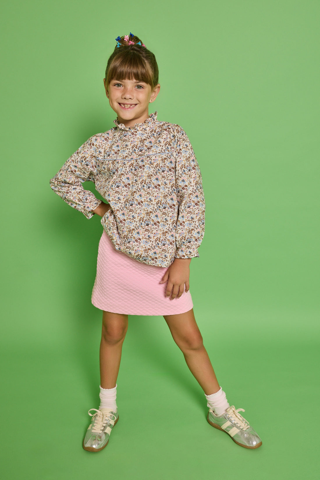 Model can be seen wearing a woven top with a ruffle neckline and button closure along back. The brown/pink/blue floral print pairs back perfectly with our quilted knit mini skirt in bubblegum pink to complete the look. 