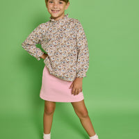 Model can be seen wearing a woven top with a ruffle neckline and button closure along back. The brown/pink/blue floral print pairs back perfectly with our quilted knit mini skirt in bubblegum pink to complete the look. 