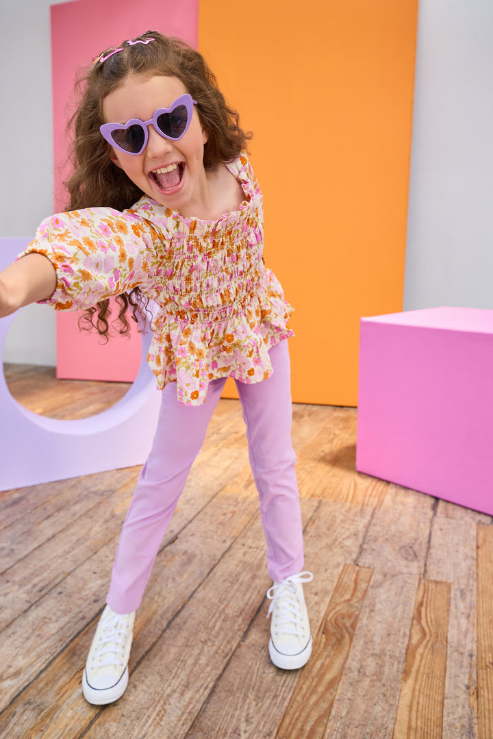 Child wearing a floral top and purple pants with colorful background