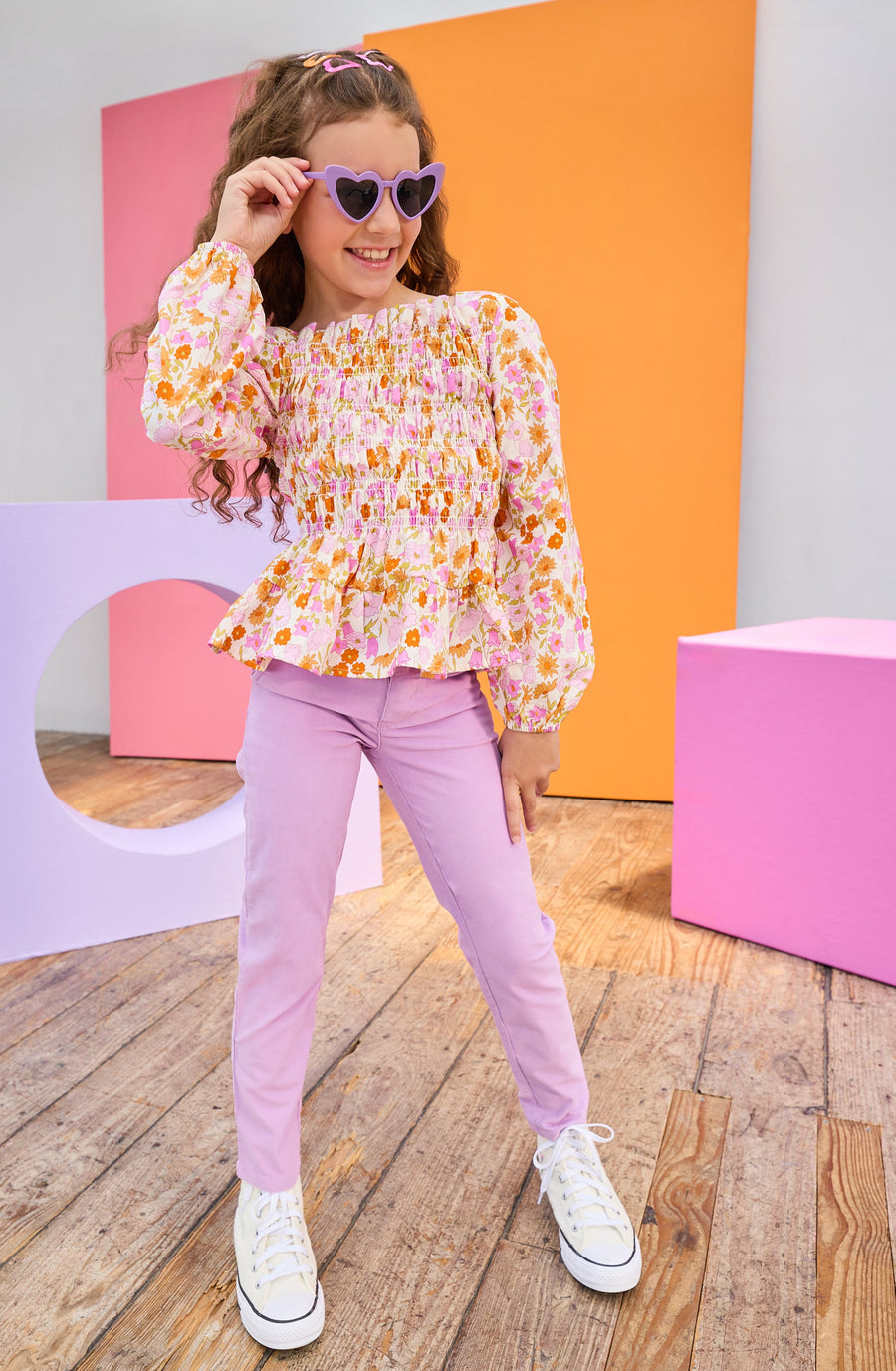Young girl in a colorful outfit with sunglasses standing in front of colorful geometric shapes.