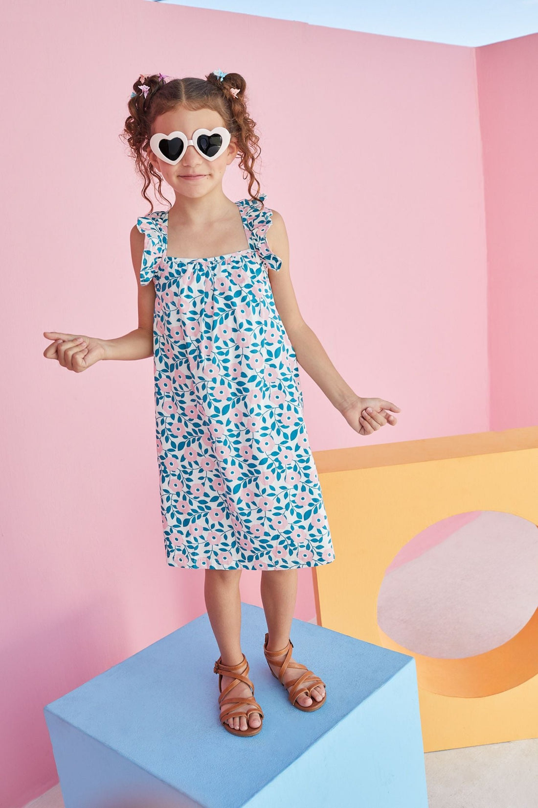 Little girl wearing ruffle strap sundress which features a square neckline and a pink and green print with flowers. 