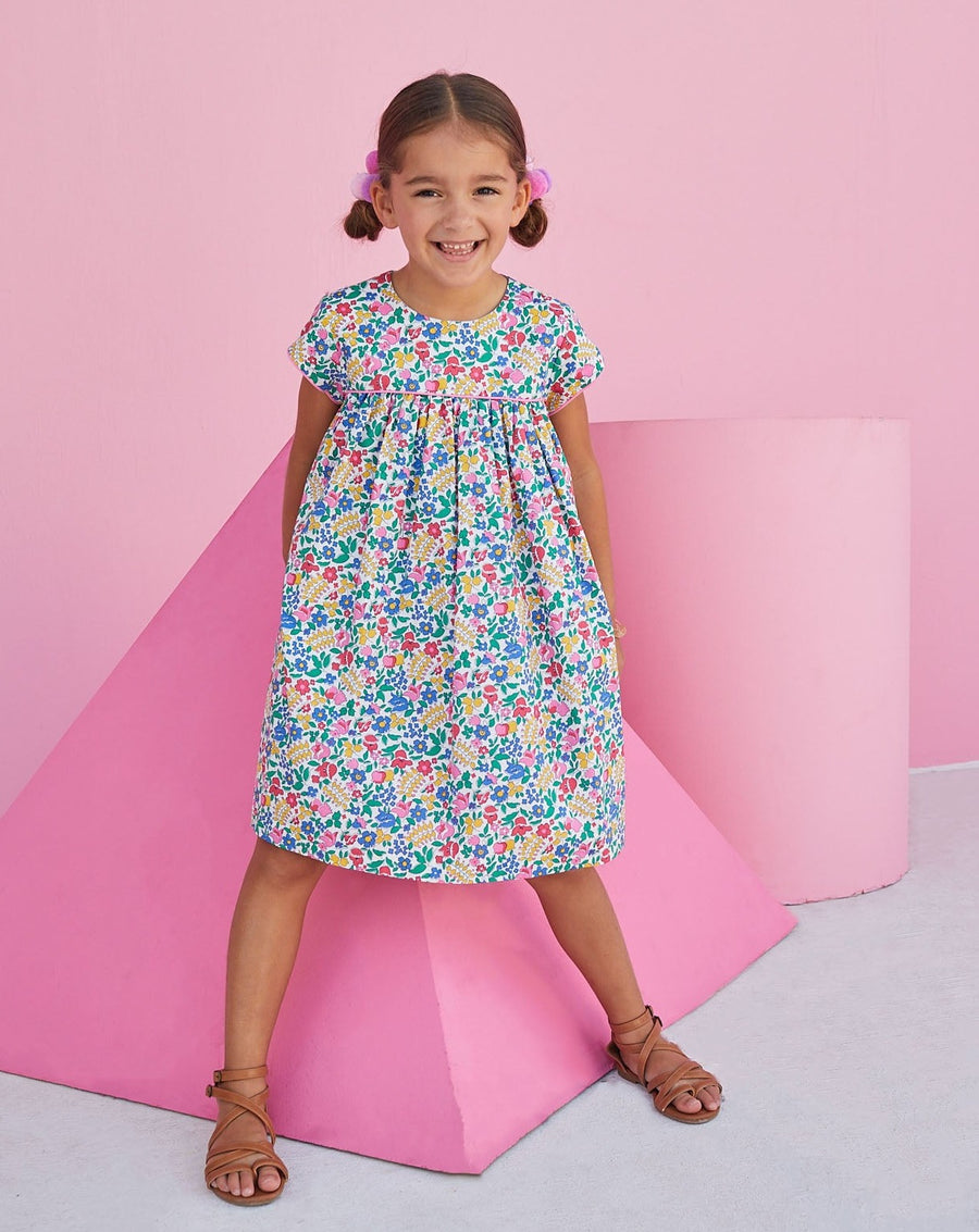 Girl wearing BISBY floral dress with pink piping and a colorful floral print.  