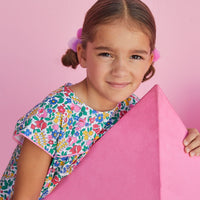 Young girl wearing BISBY Charlotte dress with vibrant flower pattern and light pink piping.