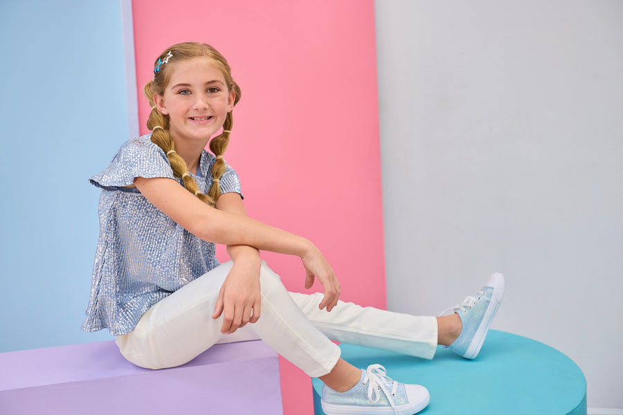 BISBY girl with braided hair sitting on a colorful platform wearing white jeans and a blue crinkle top with silver stars.