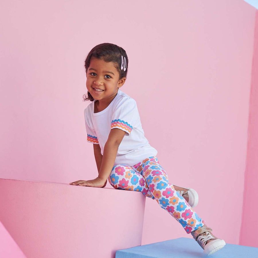 Toddler girl wearing colorful BISBY leggings in flower market pattern with pink, blue, and orange flowers.