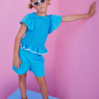 BISBY girl in our India Top in Blue which features ruching/ smocking on the body of the shirt in a super soft rayon material. Shirt is very stretchy but also form fitting and pair perfectly back with our basic shorts in Blue