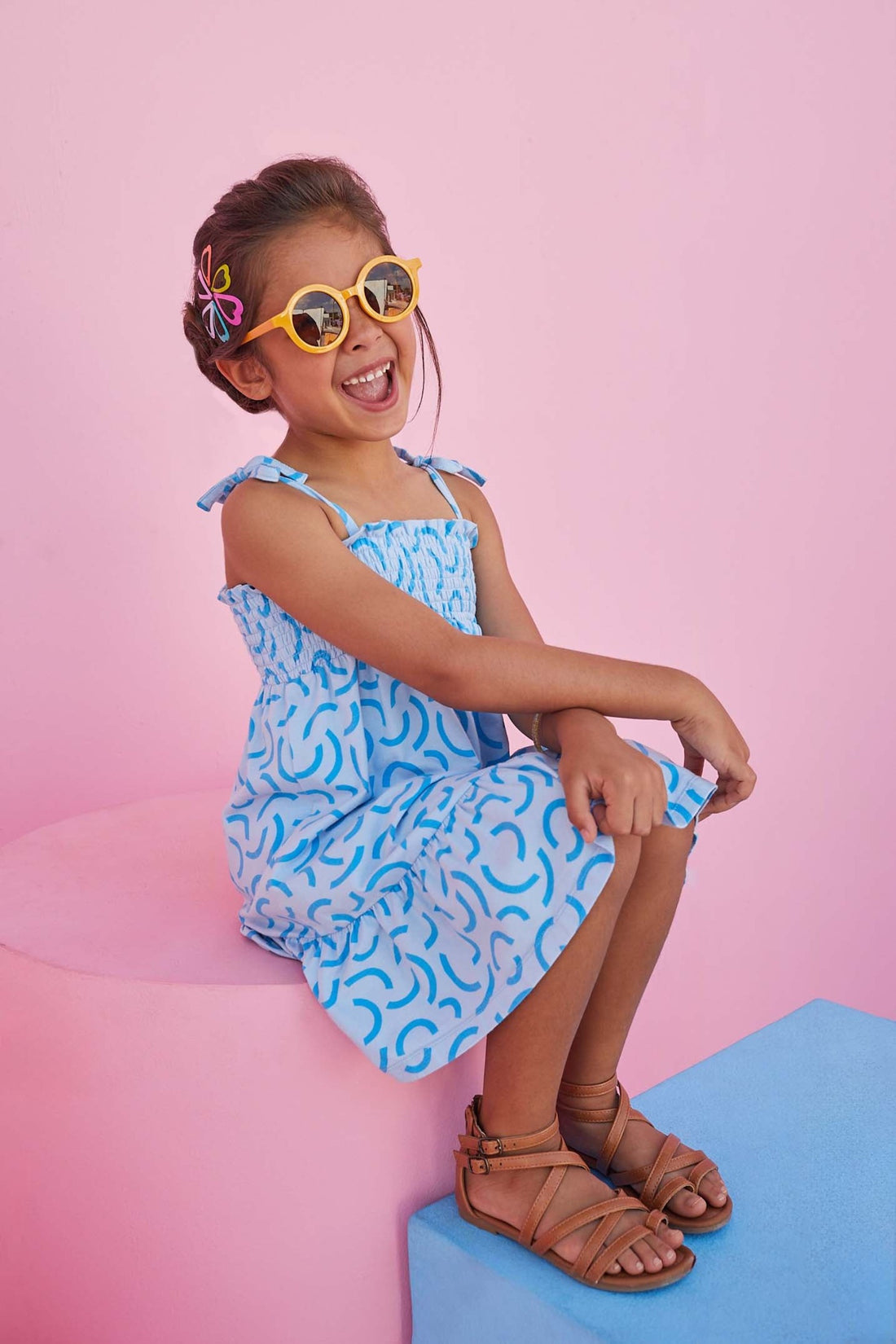 Girl smiling wearing smocked sundress with tie straps and blue details. 