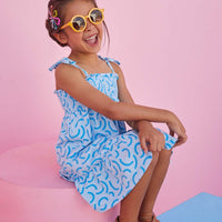 Girl smiling wearing smocked sundress with tie straps and blue details. 