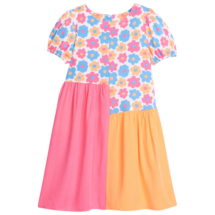 Girl asymmetrical cut dress, with top portion of dress printed in an orange, pink, and blue floral print with elastic cuffs on sleeves. The bottom half of the dress is color blocked with the right side of the dress ending in a hot pink and left side of the dress in orange. 
