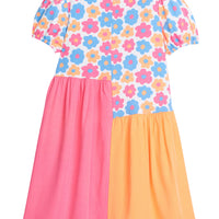 Girl asymmetrical cut dress, with top portion of dress printed in an orange, pink, and blue floral print with elastic cuffs on sleeves. The bottom half of the dress is color blocked with the right side of the dress ending in a hot pink and left side of the dress in orange. 