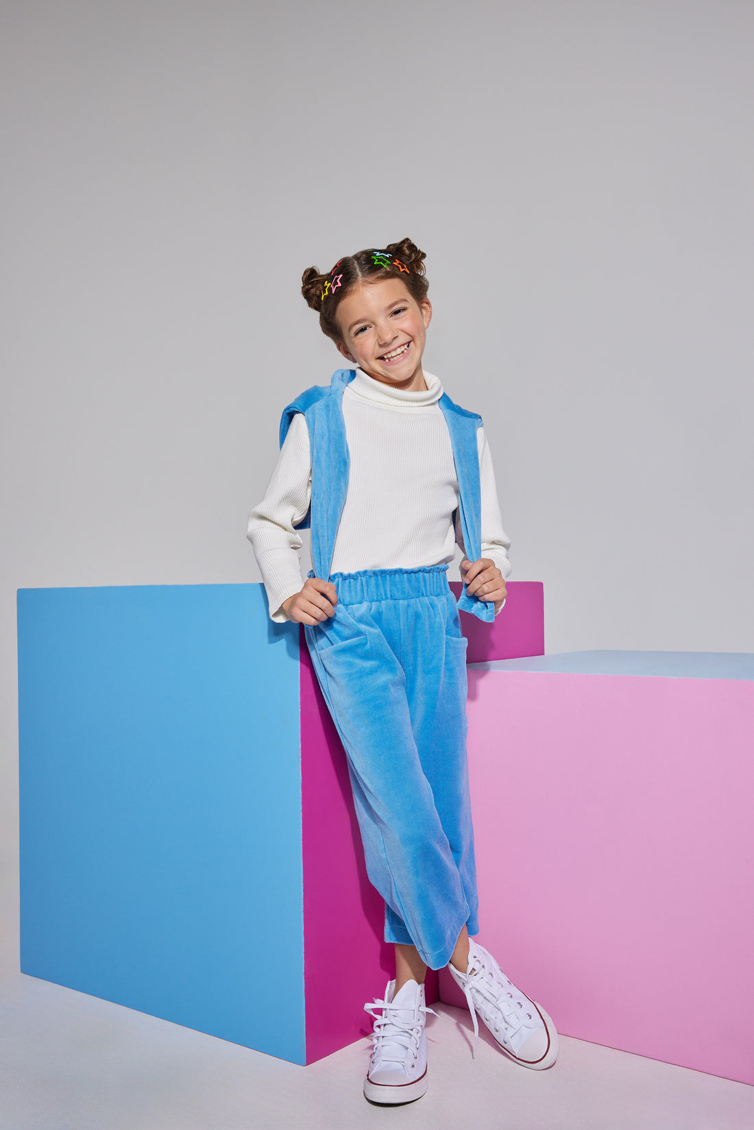 Girls/Tween ribbed turtleneck in ivory which is made of a super soft knit ribbed material and is perfect for layering. Model can be seen wearing cropped velour pants in French blue which feature an elastic waistband and pockets in the front which has a matching pullover in the same material and color thrown over the shoulders to complete the look.