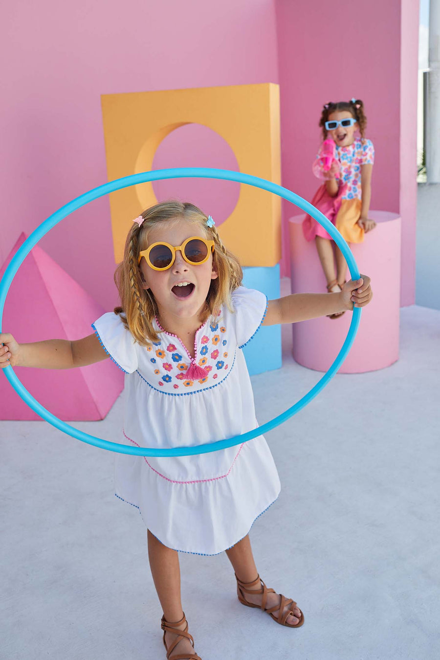 BISBY girl rocking our Positano Dress in our Flower Market Embroidery which features blue, yellow, and pink floral embroidered along the top tier of dress with fixed tassels at the end of the v-neckline. Pom poms separate each tier in blue and pink pom poms creating an elevated/fun look.