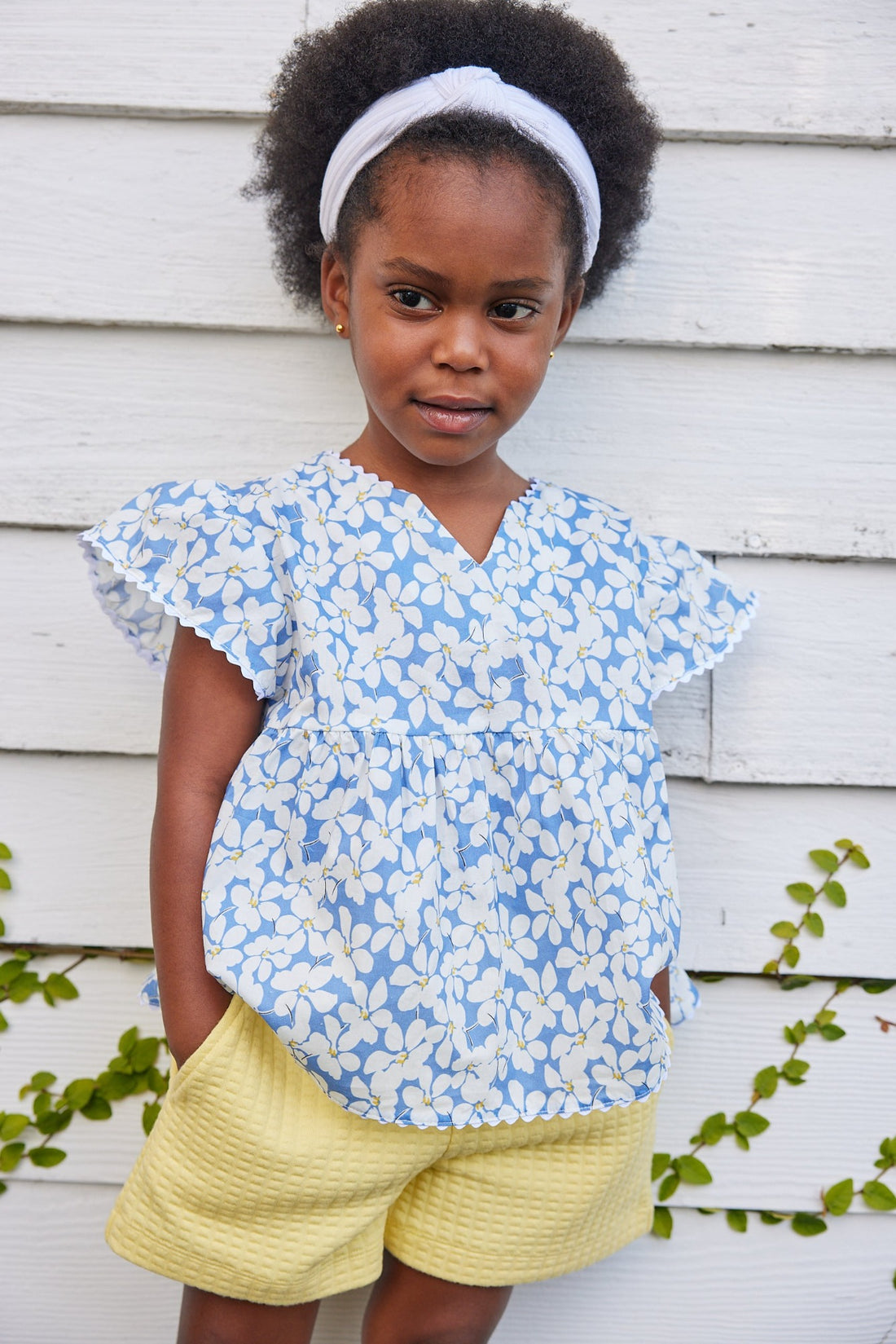 blue floral top for little girls and tweens. v-neck top with white scallop trim along sleeves and bottom of the top. Has a light blue background with white flowers