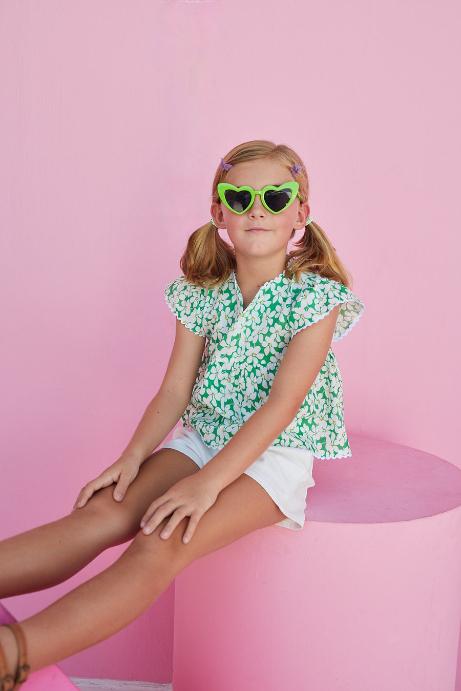 BISBY girl in our Positano Blouse in Piccadilly Lawn. A beautiful green base with white and yellow floral pattern. Shirt has scalloped edges on the sleeves and bottom of shirt and has a v-neck making it easy to get in and out of