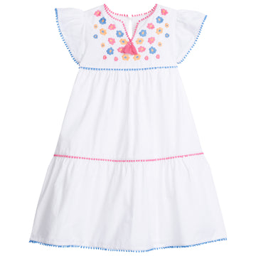 Tween girls white tiered dress with blue, pink, and orange embroidery detail on chest and hot pink tassels coming down from the v-neck neckline. Dress also features light blue pom poms along sleeve and first and bottom tiers of dress. A row of pink pom poms is seen along the second tier of dress.