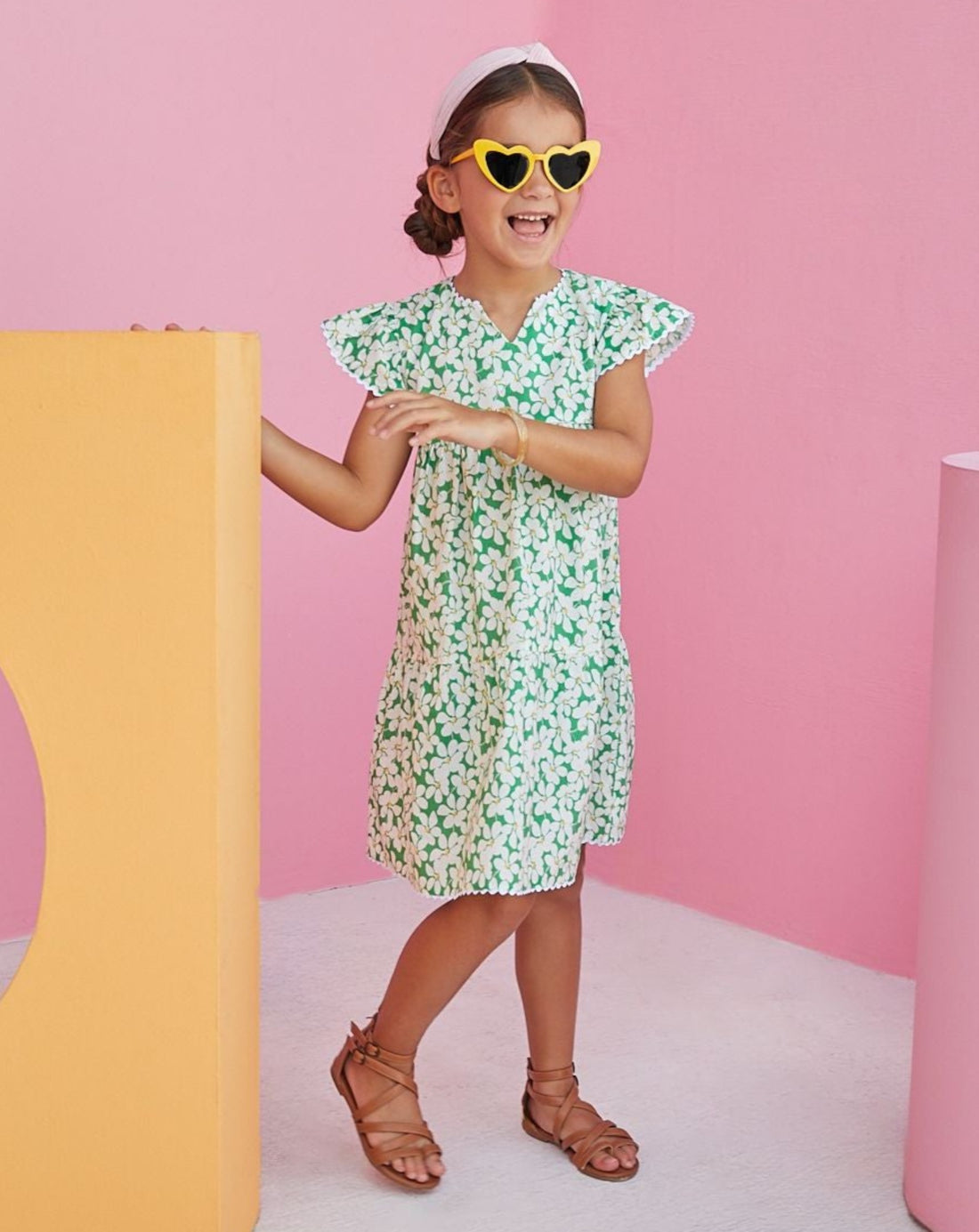 BISBY girl wearing our Positano Dress in Piccadilly Lawn. Has scalloped edges and a v-neck. The base color of dress is a beautiful green with white and yellow floral arrangement