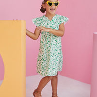 BISBY girl wearing our Positano Dress in Piccadilly Lawn. Has scalloped edges and a v-neck. The base color of dress is a beautiful green with white and yellow floral arrangement