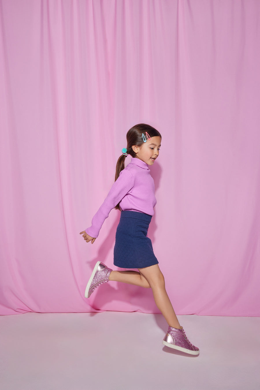 Girls/Tween ribbed turtleneck in a purple petal shade. Turtleneck is made of a super soft/stretchy/thick material so it is perfect for fall and winter. Model can be seen wearing a quilted navy skirt to complete the look. 