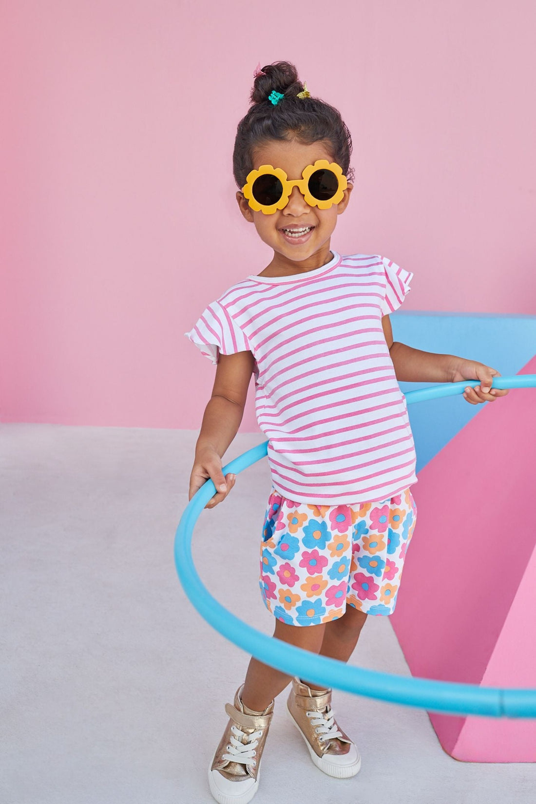 Model wearing BISBY Rosie Short Set in flower market print of pink, blue, and orange flowers, and a top with pink and white stripes and flutter sleeves. 