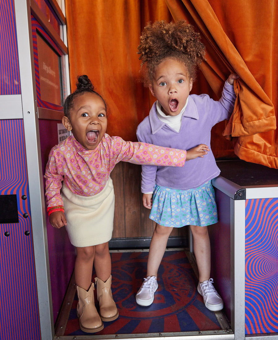 Little girl can be seen wearing our Lilac Polo pullover layered with our Cream colored essential turtleneck underneath paired with our skirt in Seville Azul. Little girl on left can be seen wearing our Seville Rose turtleneck paired with our Mini Sherpa skirt--BISBY girl