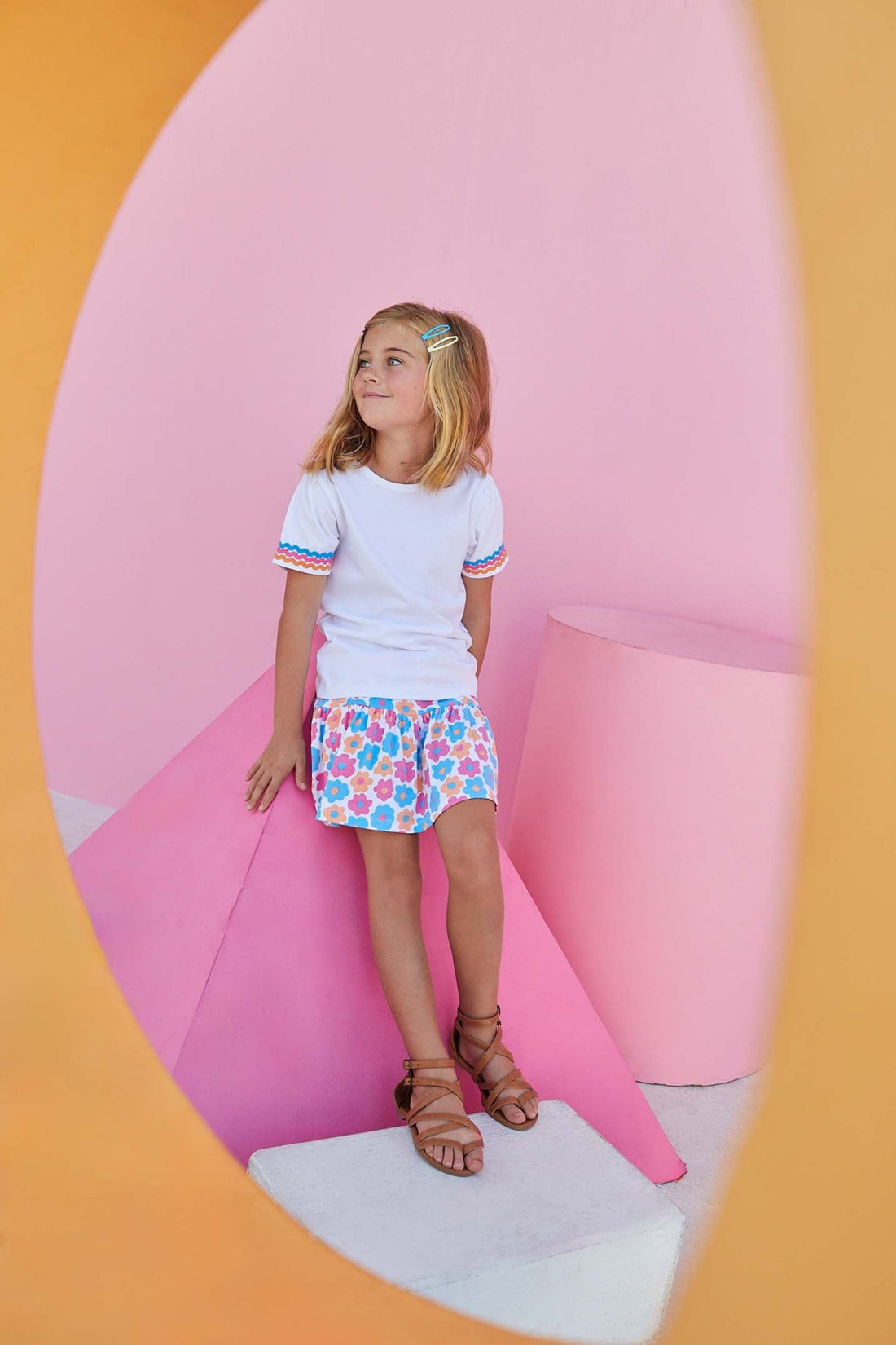 Little girl smiling and wearing our short sleeved white tee with three colors of ric rac detailing on the sleeve in blue, pink, and orange.