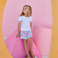 Little girl smiling and wearing our short sleeved white tee with three colors of ric rac detailing on the sleeve in blue, pink, and orange.