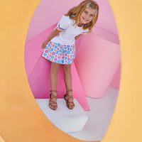 Smiling girl wearing vibrant sally skort featuring blue, pink, and orange flowers. 