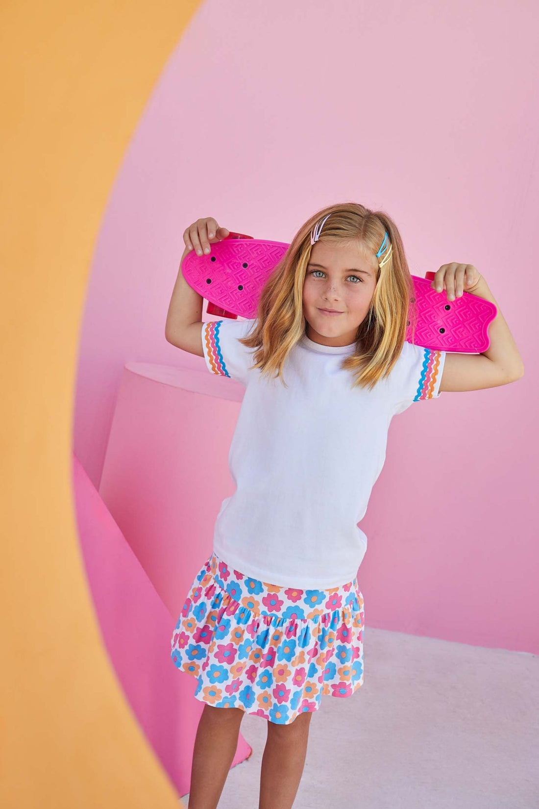 Little girl smiling and wearing our sally skort in the flower market print which has pink, blue, and orange flower print on it. The skort is knit and very comfortable. 