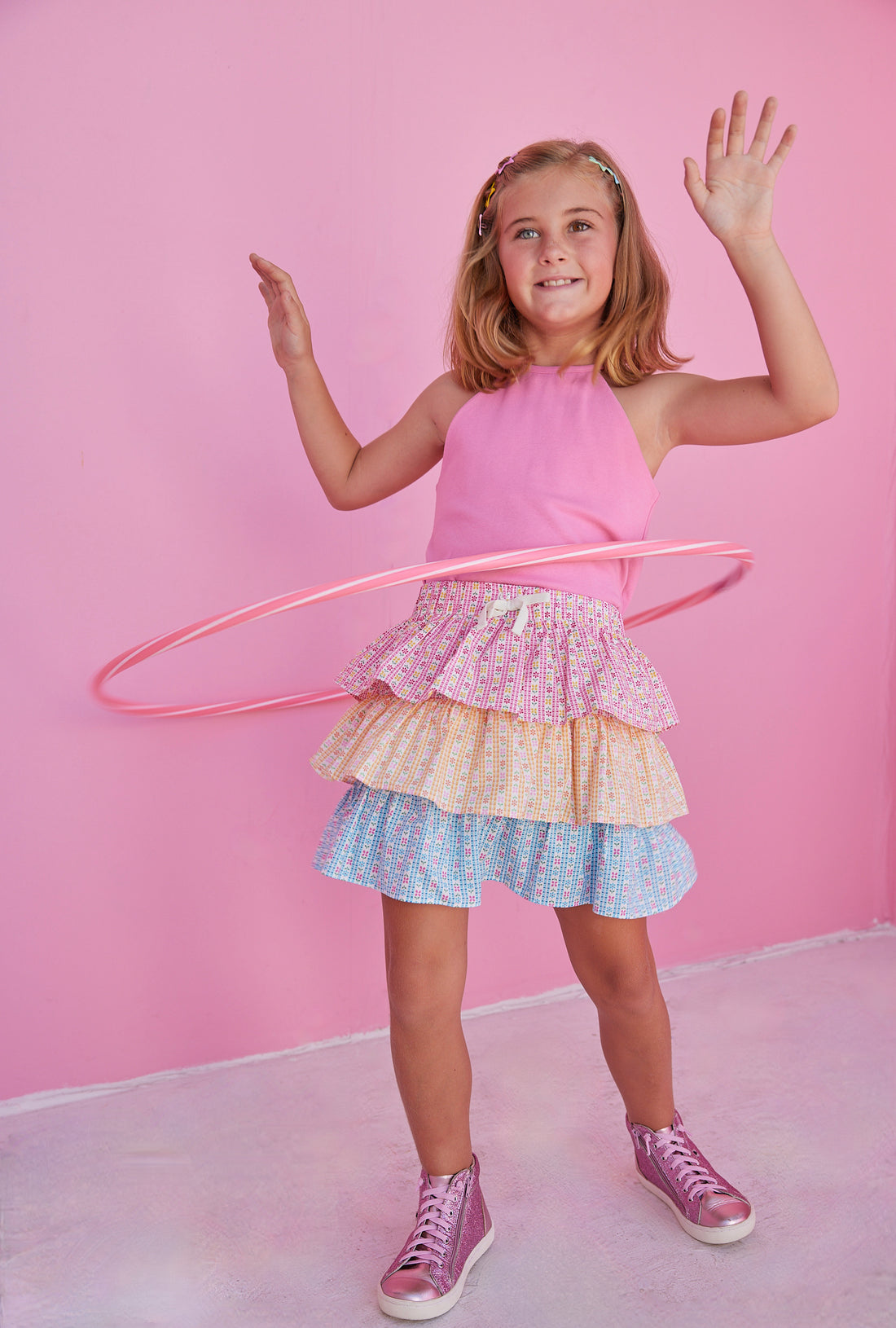 BISBY girl in our Tiered Mini Skort in our "Daisy Chain" with top tier in pink, middle tier in orange, and bottom tier in blue floral pattern. Skort has built in shorts and has elastic waistband. Paired perfectly with our Hot pink halter top