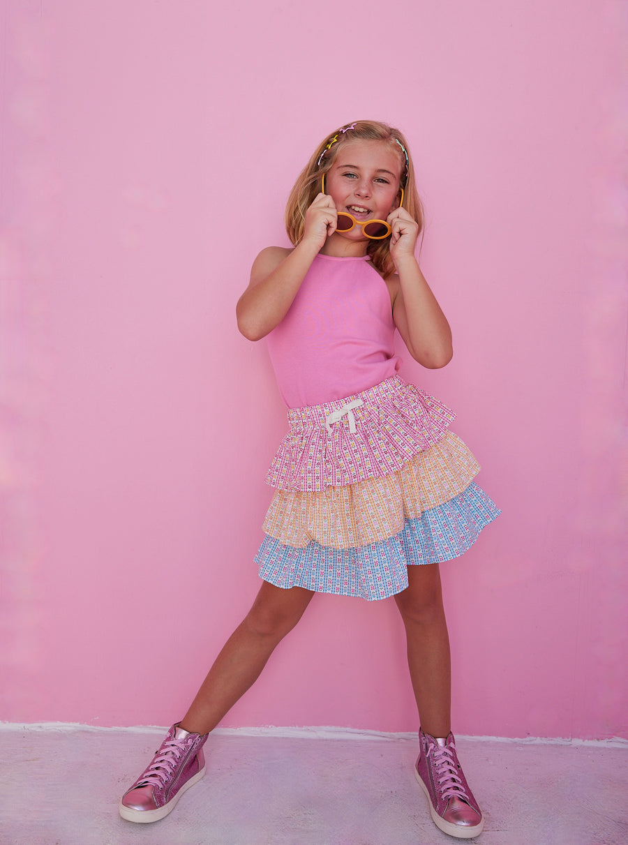 BISBY girl in our Tiered Mini Skort in our "Daisy Chain" with top tier in pink, middle tier in orange, and bottom tier in blue floral pattern. Skort has built in shorts and has elastic waistband. Paired perfectly with our Hot pink halter top