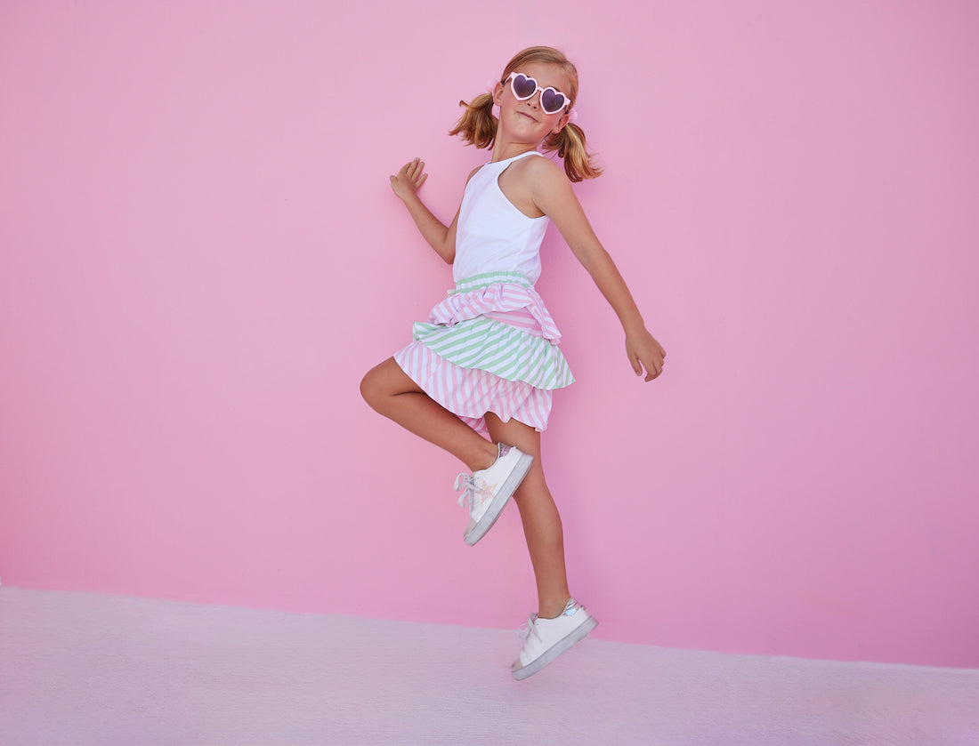 BISBY girl in our Tiered Mini Skort in Pink & Green Stripe which features pink and green tiers with a fixed tie and elastic waistband. These shorts are also perfect for your active girl because they have built in shorts as well. Pair it back with our halter top in white for a fun elevated look.