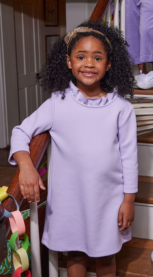Little girl can be seen wearing our Lilac Tory Dress with ruffles around neckline--BISBY girls