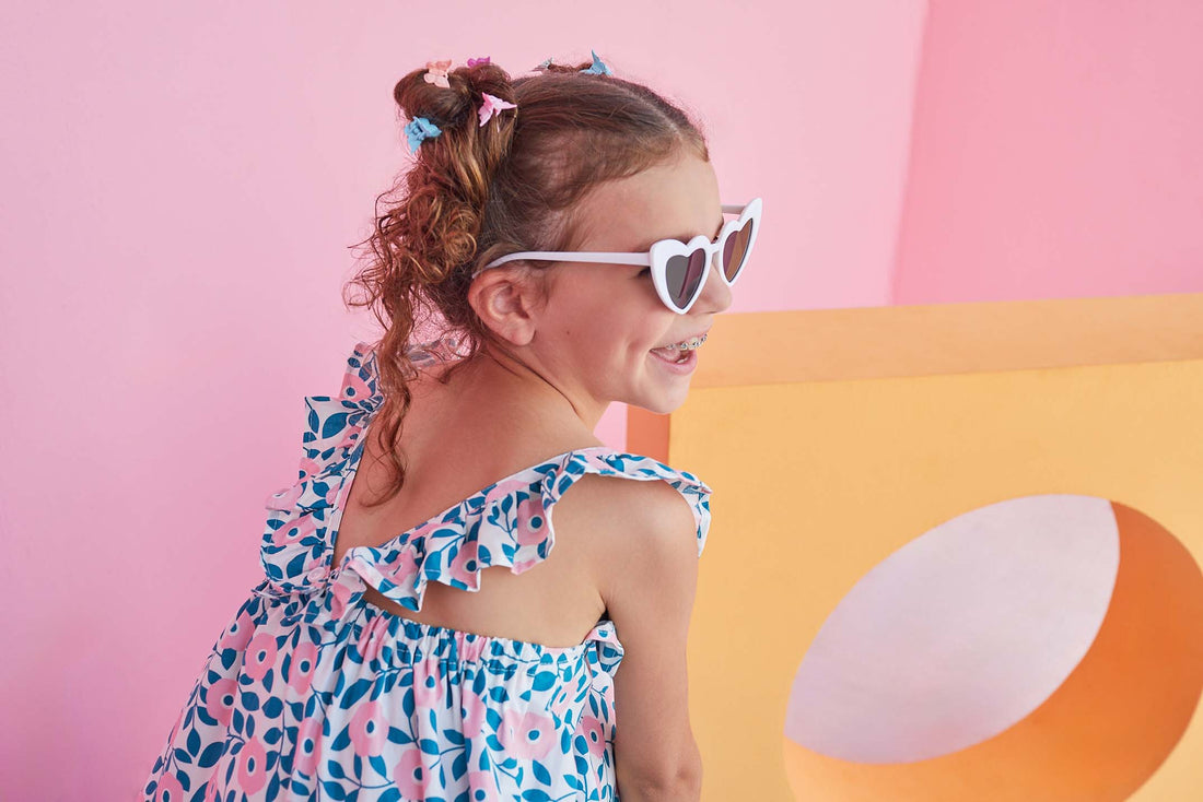 Little girl seen from the side wearing our Tribeca dress which features V ruffled staps in the back and a print with blue leaves and light pink flowers