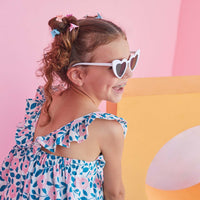 Little girl seen from the side wearing our Tribeca dress which features V ruffled staps in the back and a print with blue leaves and light pink flowers