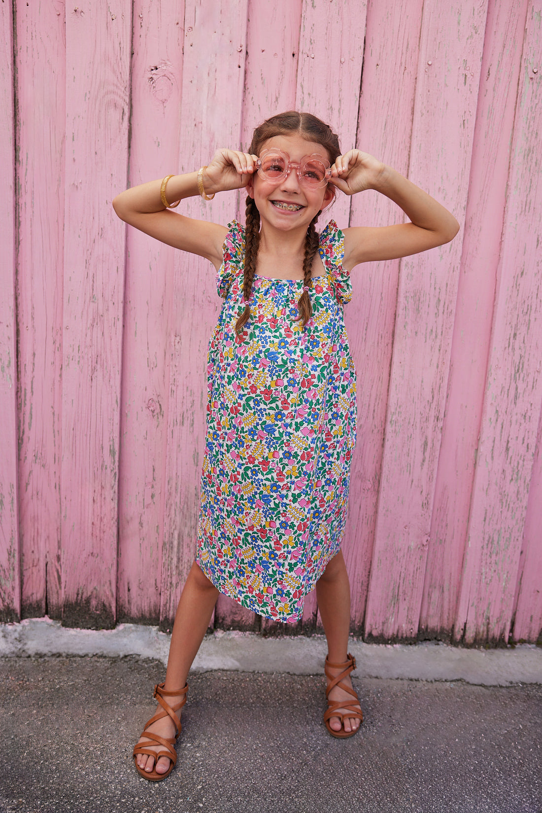 Little girl wearing ruffle adjustable strap sundress which features a square neckline and a colorful floral print. 