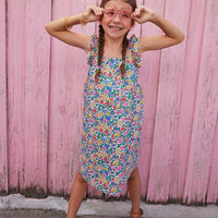 Little girl wearing ruffle adjustable strap sundress which features a square neckline and a colorful floral print. 
