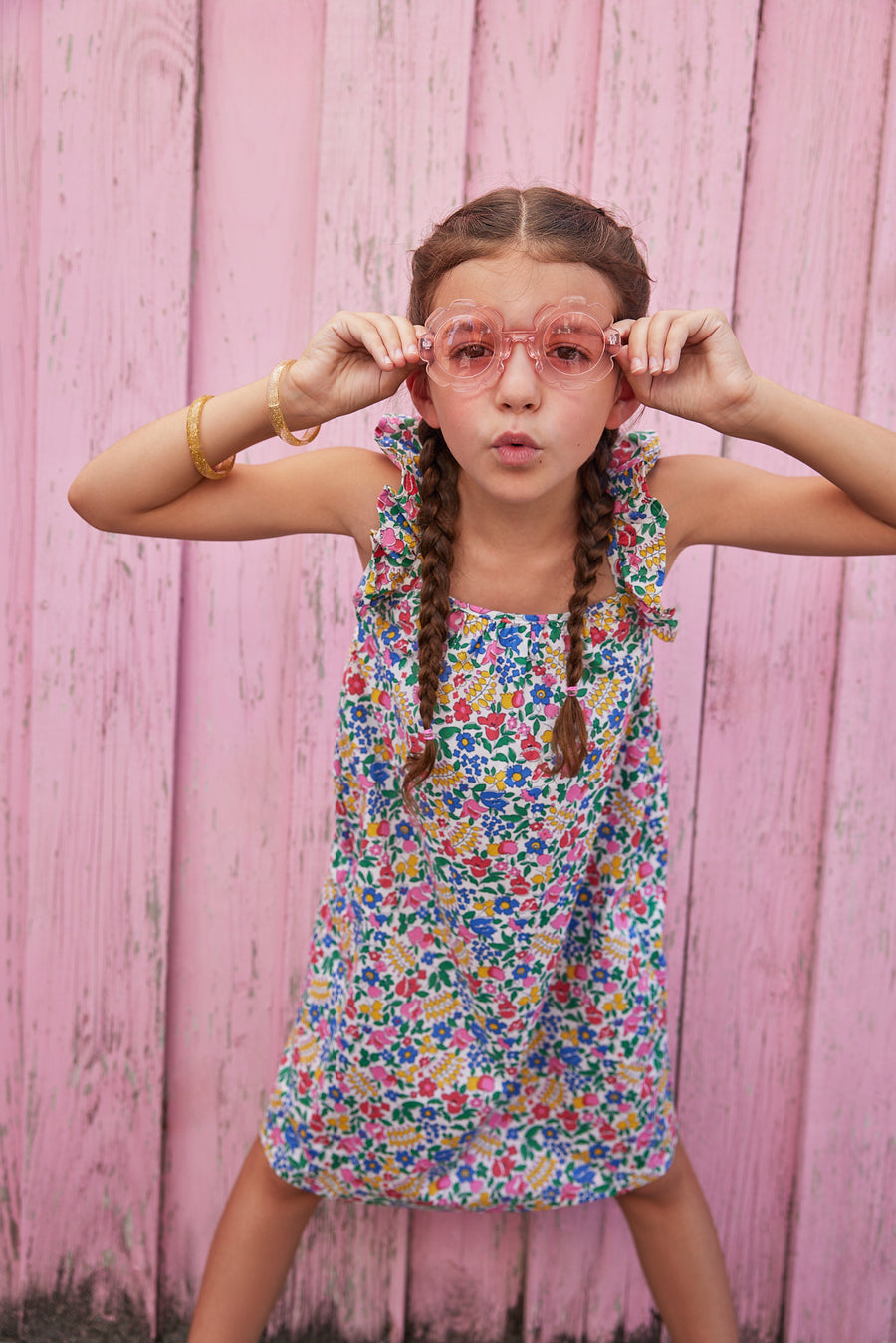 Little girl wearing ruffle adjustable strap sundress which features a square neckline and a colorful floral print. 