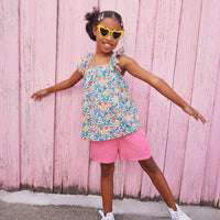 Little girl wearing ruffle adjustable strap top which features a square neckline and a colorful floral print. 