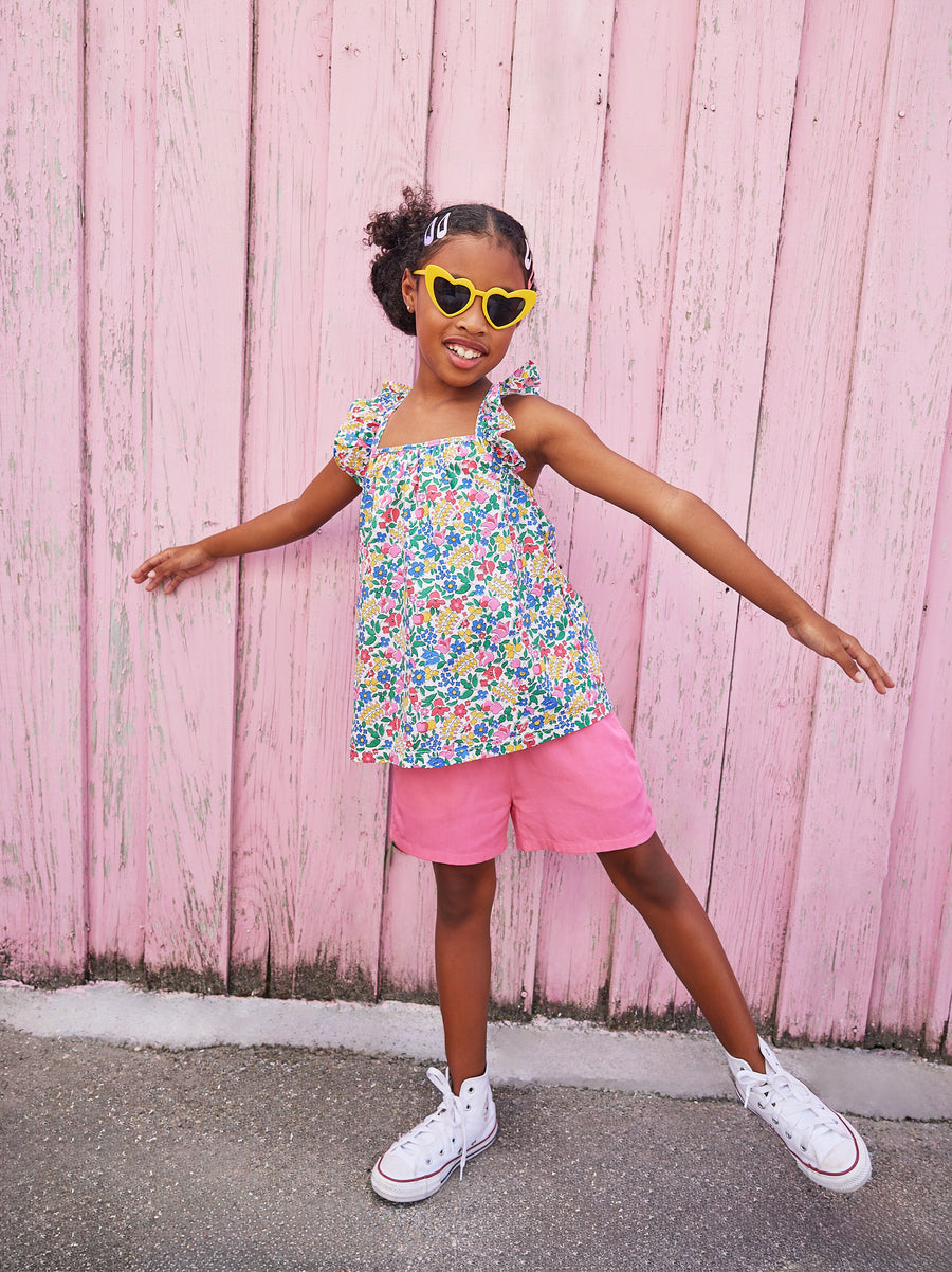 Little girl wearing ruffle adjustable strap top which features a square neckline and a colorful floral print. 