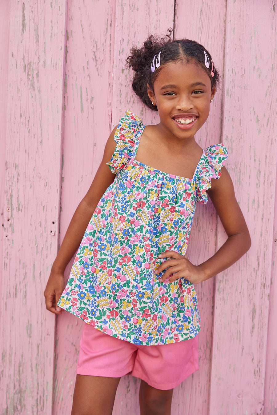Little girl wearing ruffle adjustable strap top which features a square neckline and a colorful floral print. 