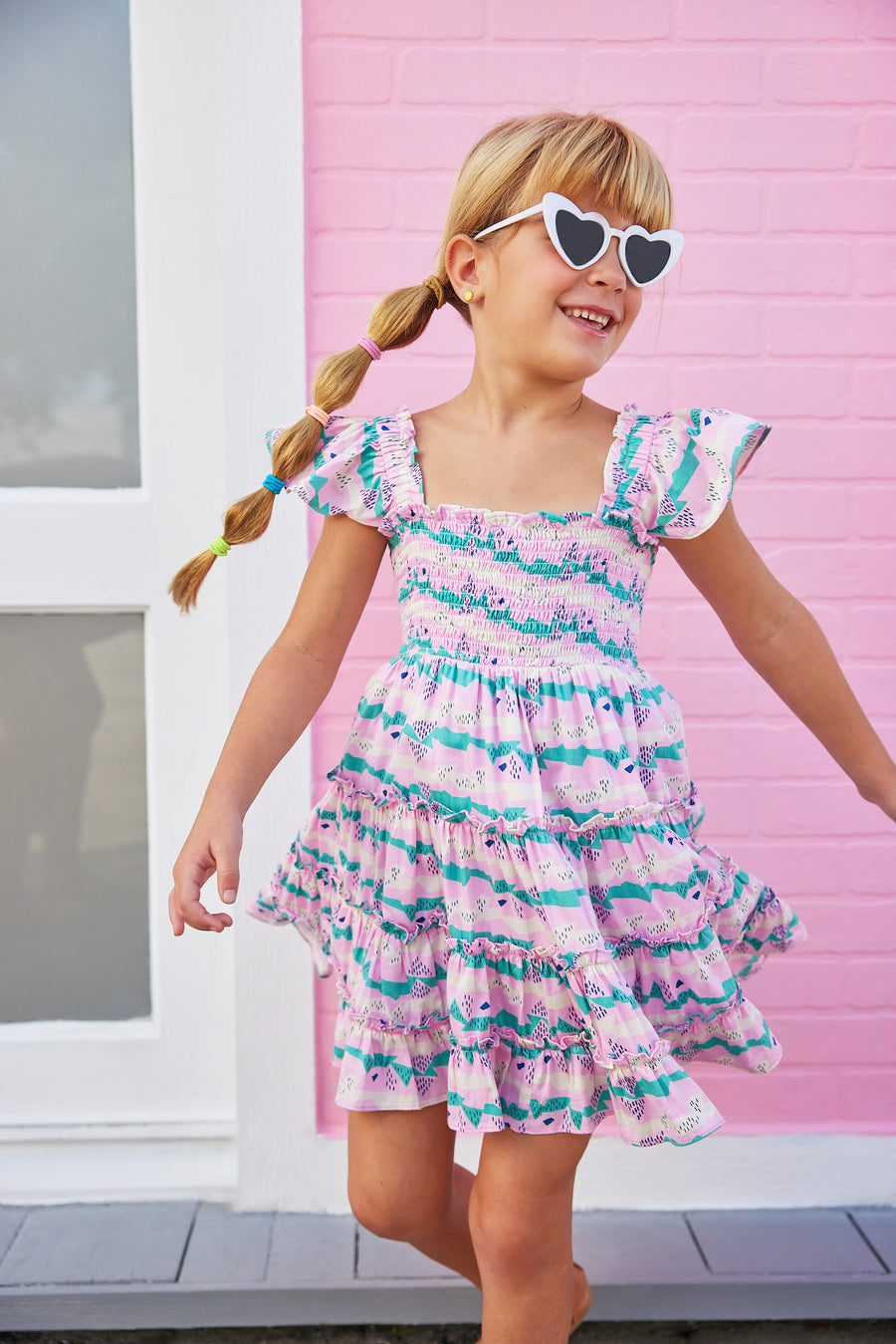 BISBY girl in our new Twirl Dress in our Alli Stripe. This dress features smocking on the bust and has angel sleeves for a more elevated look. Made from a super soft material, this pink/green/ and cream dress is the perfect, comfortable, flowy dress for summer.