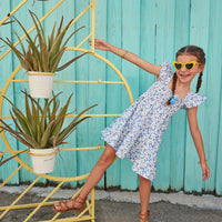 Girl/tween dress with ruffle sleeves and ruching across bust, also features a light blue background with white flowers and yellow centers printed cross body of dress.