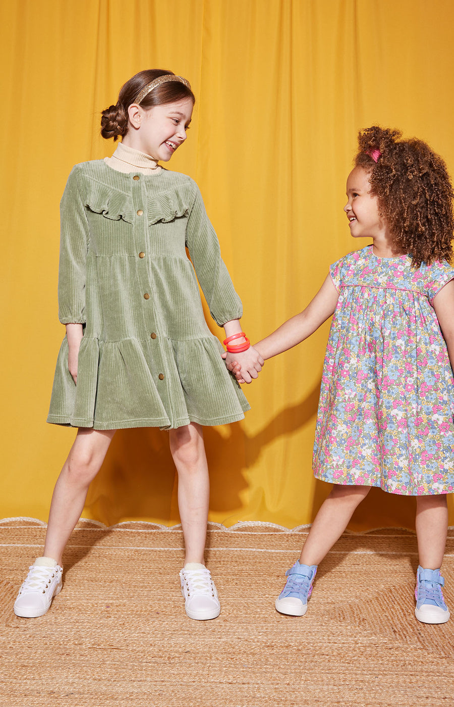 Little girls can be seen wearing two popular dresses. On left, wearing our Sage Corduroy Western Styled dress paired with tan turtleneck (left) and the other little girl wearing the Charlotte Merion Floral Dress--BISBY girl