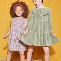 Little girls can be seen wearing two popular dresses. On left, wearing our Sage Corduroy Western Styled dress paired with tan turtleneck (right) and the other little girl wearing the Charlotte Merion Floral Dress--BISBY girl