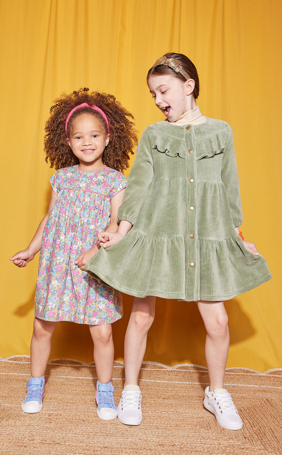 Little girls can be seen wearing two popular dresses. On left, wearing our Sage Corduroy Western Styled dress paired with tan turtleneck (right) and the other little girl wearing the Charlotte Merion Floral Dress--BISBY girl