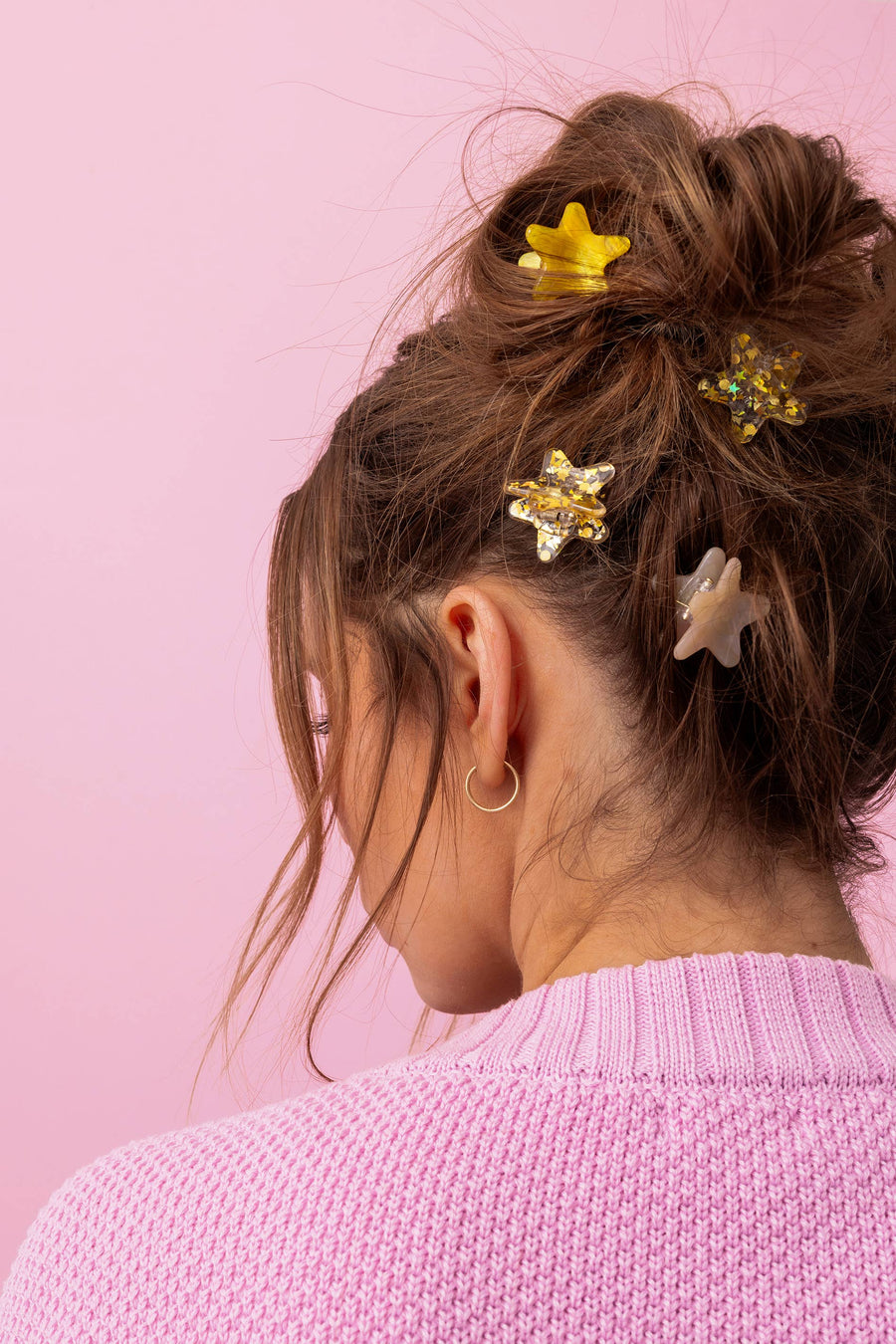 Person with hair styled with star hair clips against a pink background