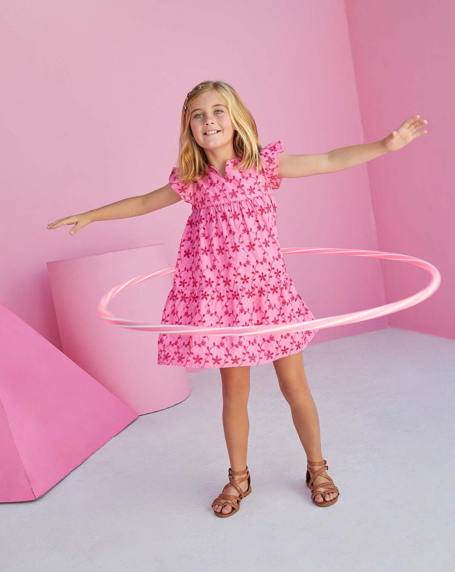 Young girl hula hooping in a babydoll pink eyelet dress with flutter sleeves. 